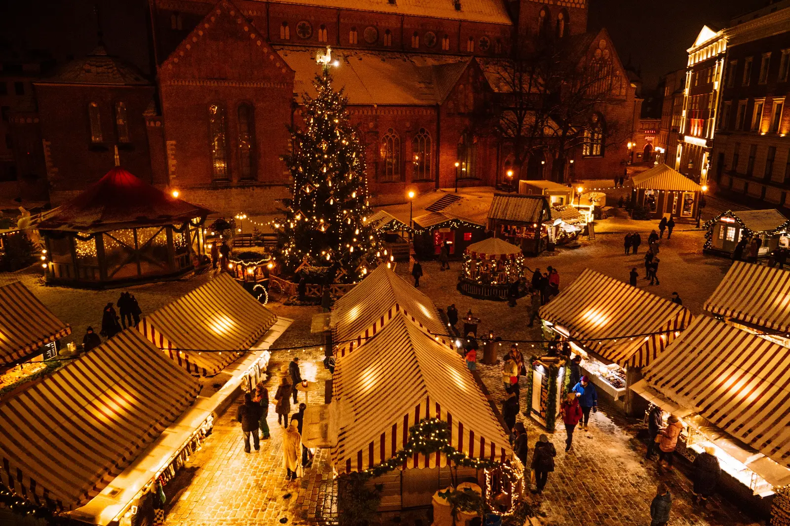 Festive Christmas market stalls in a European city square at night with lights and decorations